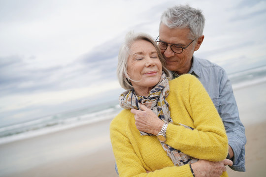 Portrait of attractive vibrant senior couple embracing on beach in fall