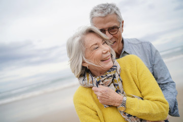 Portrait of attractive vibrant senior couple embracing on beach in fall