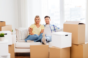 mortgage, moving and real estate concept - happy couple with boxes resting on sofa at new home