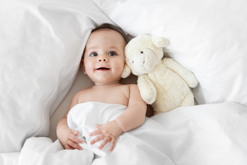 Cute baby lying on white bed with stuffed animal