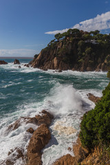 Rocky coastline and crashing waves of the Costa Brava, Spain, against blue sky