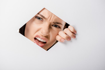 angry young woman looking at camera through hole on white