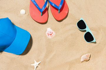Fototapeta na wymiar vacation and summer holidays concept - cap, flip flops, sunglasses and seashells on beach sand