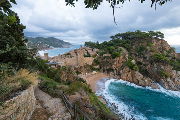 Beach and the fortress of Tossa de Mar, Spain, against cloudy sky