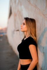 Sideways portrait of beautiful blonde woman in black top near wall