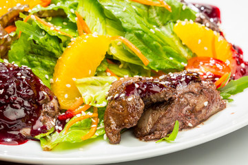 Salad with beef tenderloin, salad leaves, tomatoes, oranges, sesame. On a white plate and a white background
