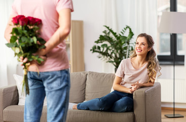 couple, relationships and people concept - happy woman looking at man with bunch of flowers at home