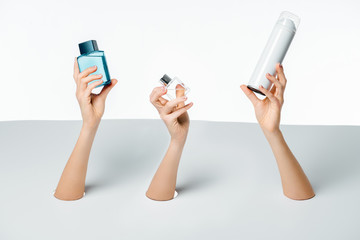 cropped shot of female hands holding perfumes through holes on white