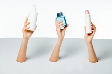 close-up partial view of women holding beauty products through holes on white