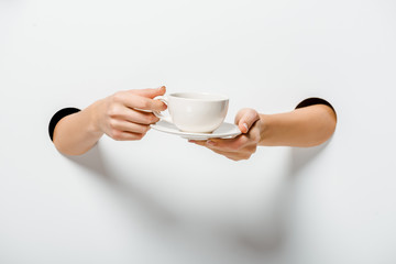 cropped image of woman holding cup of coffee and plate through holes on white
