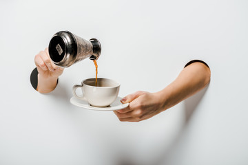 cropped image of woman pouring coffee from cezve into cup through holes on white