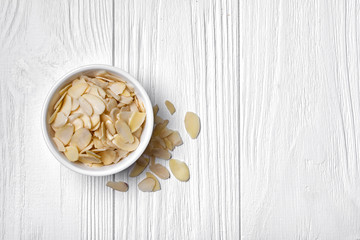 Fototapeta na wymiar Top view of almond slices in white bowl on wooden background