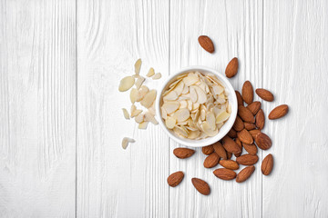 Top view of almond slices and whole nut in white bowl on wooden background