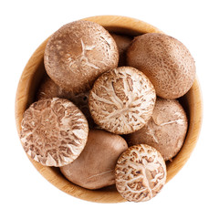 Fresh shiitake mushrooms in wooden bowl isolated on white. Top view.