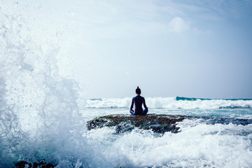 Woman meditation at the seaside cliff edge facing the coming strong sea waves