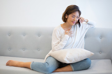 Portrait of smiling young woman talking on phone to friend. Asian girl sitting on coach and using smartphone at home. Wireless communication concept