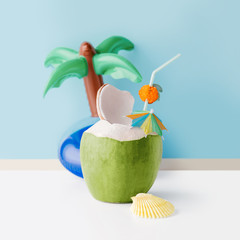 Fresh coconut on a pastel blue background with coconut tree inflatable drink holder, summer vibes...