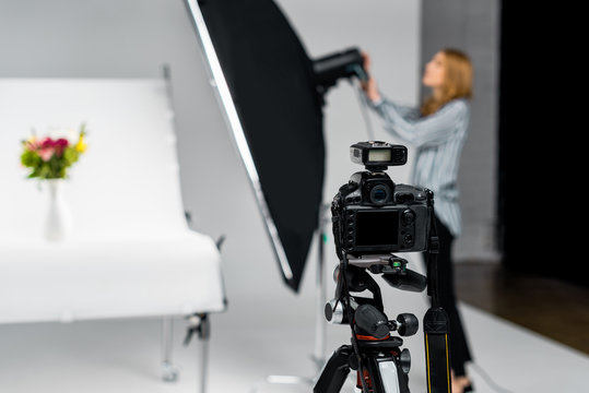 close-up view of photo camera and young woman working with lighting equipment in studio