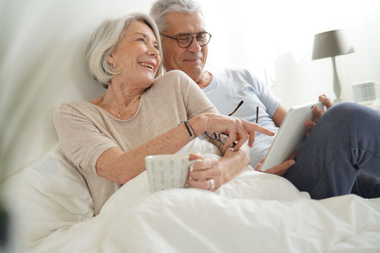   Senior couple relaxing in bed looking at tablet