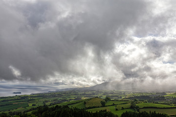 Rain falls in the distance on pasture and farm land above Vila Franca do Campo in Sao Miguel, Azores.