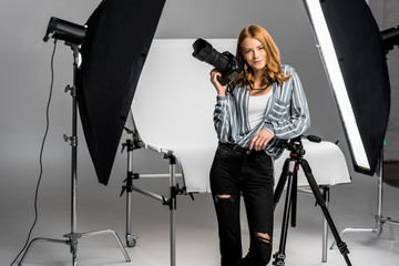 attractive young female photographer working in professional photo studio - obrazy, fototapety, plakaty
