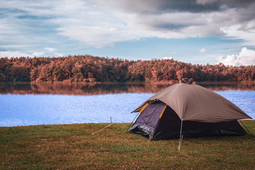 A camping site by a lake with a tent and a forest line with autumn colors of the leaves on the trees on the other side of the lake