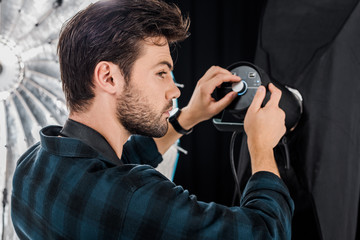 young photographer working with professional lighting equipment in photo studio