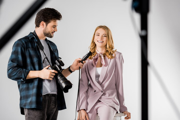 smiling young photographer holding camera and light meter while working with model in studio