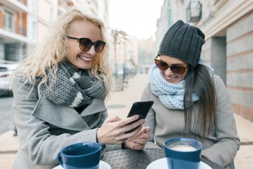Two young smiling fashionable women having fun in outdoor cafe. Urban background, women laughing...