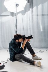 handsome young photographer with professional camera taking pictures in studio