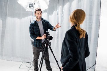 smiling young photographer using camera and talking with female model in studio