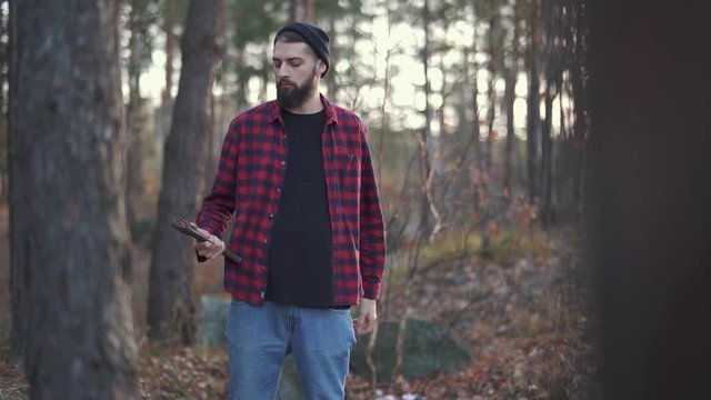 Bearded guy play with his axe, guy throw ax from one hand to another. Brutal man with an axe outdoors.