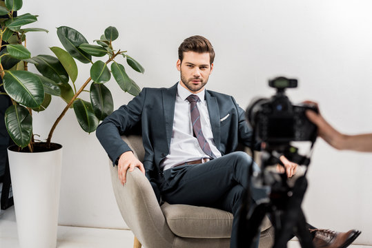 cropped shot of photographer taking pictures of handsome man in stylish suit in studio
