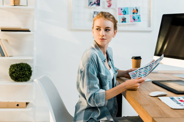 beautiful young retoucher working with photos and looking away in office