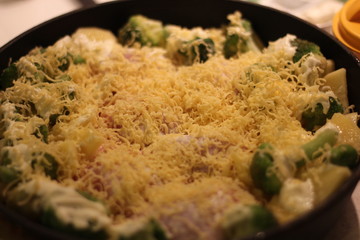Cooking vegetarian dish with broccoli and potatoes covered with grated cheese before baking, healthy concept.