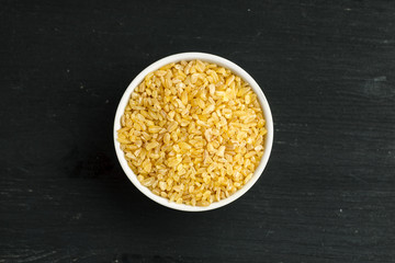 Bulgur in a white bowl on a black wooden table, top view