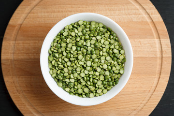 Dry green peas in a white bowl on a wooden table, top view
