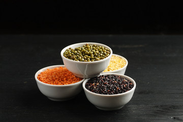 Set of different cereals and legumes in a white bowls on a black table