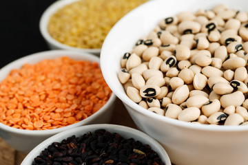 Set of different cereals and legumes in a white bowls on a black table