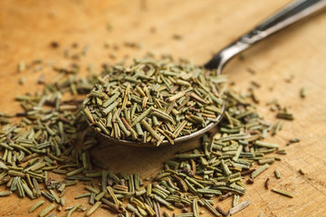 Dry rosemary in metal spoon on a wooden table