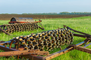 The cambridge roller is on the green grass near the cultivated field