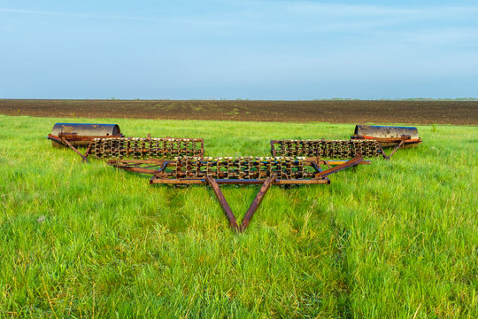 The cambridge roller is on the green grass near the cultivated field