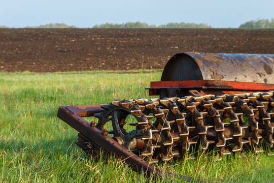 The cambridge roller is on the green grass near the cultivated field