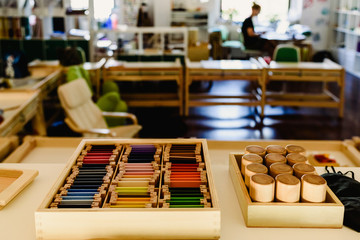 Table and shelving with montessori material, colored items and wooden cylinders to study geometry in the classroom.