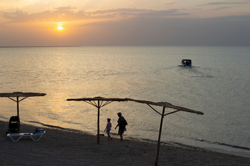 Sunset on the sea, people leave the beach in the evening and the boat sails from the shore of the...