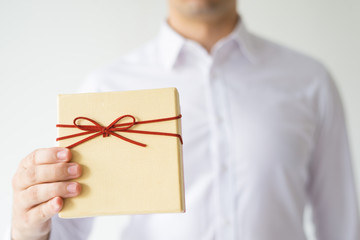 Closeup of man wearing white shirt and holding gift box. Person greeting someone. Gift concept. Isolated cropped front view on white background.