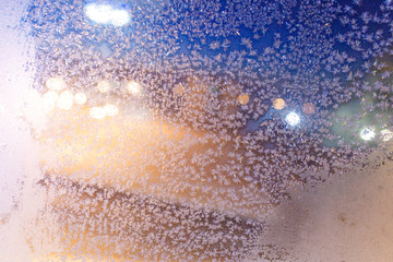 Frosty pattern on the glass. The figure is made of cold air. Colored bokeh spots