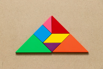 Color tangram puzzle in triangle shape on wood background