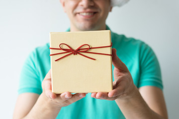 Closeup of smiling guy holding gift box. Man wearing t-shirt. Gift concept. Isolated cropped front view on white background.