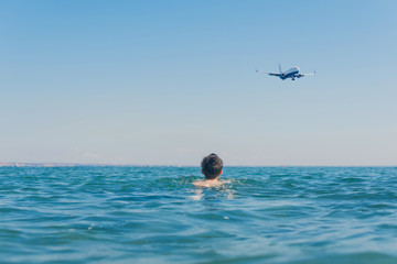 Fototapeta na wymiar 13 years old boy in the sea waves under landing plane. Concept of family summer vacation